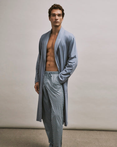 Man wearing a light blue robe over patterned pants on a neutral background